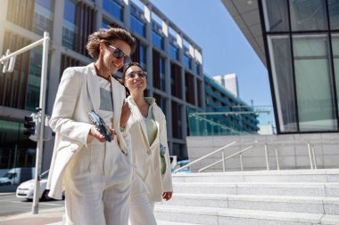 Moda kıyafetleri içinde kadınlar gülüyor ve iş merkezinin yakınına yürüyorlar. Bulanık arkaplan