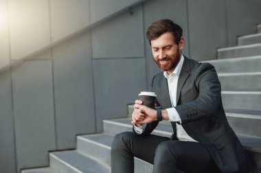 Businessman in suit sitting on stairs with coffee during break. Blurred background