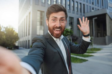 Happy businessman in suit make a selfie on background of his office building. Bussines concept