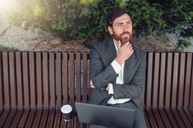 Male businessman working on laptop at lunchtime sitting on bench near office. Blurred background