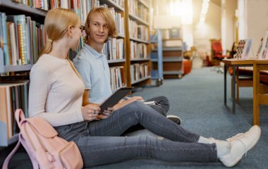 Friends student sit on floor near bookshelves in library and studying. Education concept