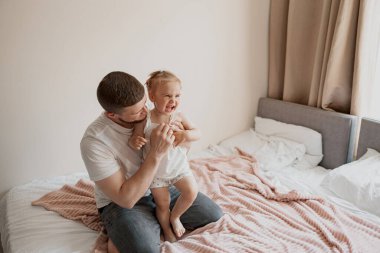 Daddy playing with dauther at home sitting on the bed. High quality photo