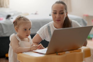 Mom and daughter spending leisure time and watching cartoons on laptop at home. Blurred background