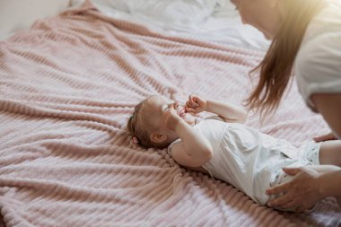 Young mother smiling and playing with her baby while lying in bed at home. Blurred background
