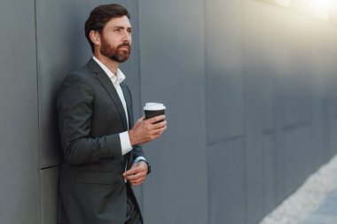 Businessman in suit drinking coffee near office building. Business concept