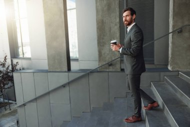 Handsome businessman goes down stairs with coffee during break near office. Blurred background