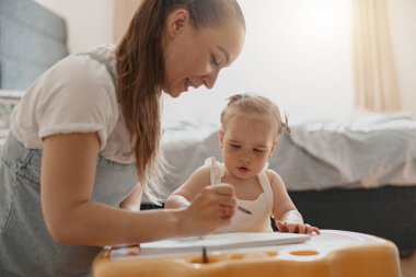 Little girl painting with her mother at home while spending time together. High quality photo