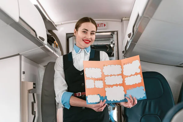 Smiling Female Flight Attendant Holding Instruction Booklet Standing Board — Stock fotografie