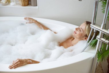 Top view on young blonde attractive female lying in hot bathtub and relaxing in bubbles. Relaxation.