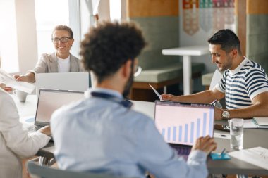 Diverse coworkers analyzing sales report while working together in office. Blurred background