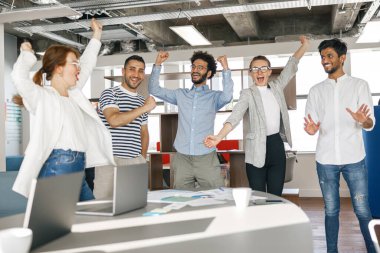 Happy group of businesspeople laughing cheerfully and raised their hands up in a modern workplace