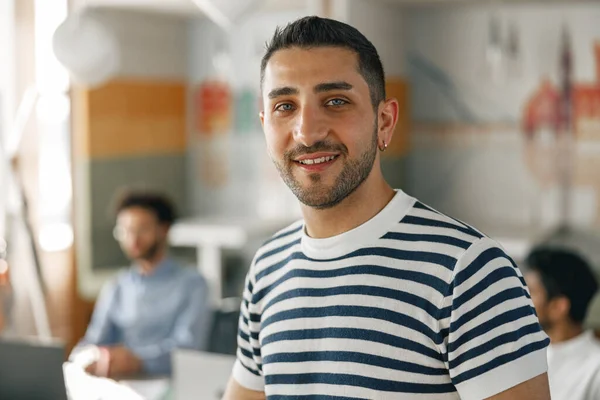 Smiling businessman in casual clothes standing in modern office on colleagues background