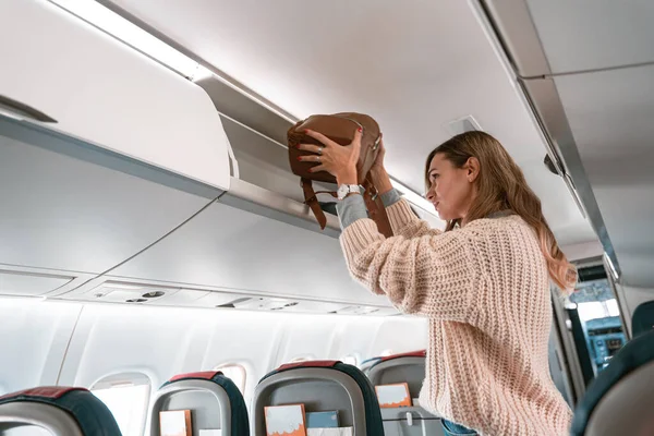 Yolcu kadın, uçağa binerken bavullarını üst kattaki dolaba koyuyor. Yüksek kalite fotoğraf