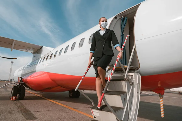 Woman flight attendant in mask standing on airplane stairs at airport