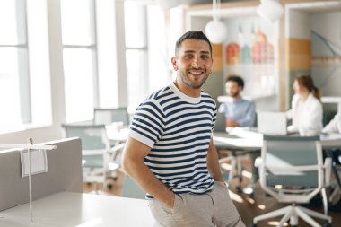 Smiling businessman in casual clothes standing in modern office on colleagues background