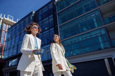 Moda kıyafetleri içinde kadınlar gülüyor ve iş merkezinin yakınına yürüyorlar. Bulanık arkaplan