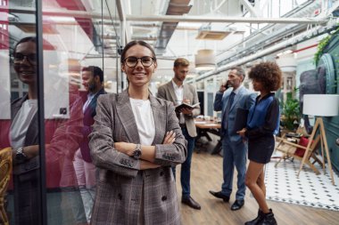 Smiling businesswoman standing in modern office on colleagues background and looking camera