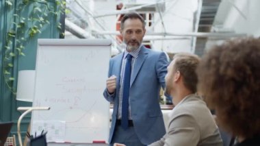 Mature coach or speaker make flip chart presentation to diverse businesspeople at meeting