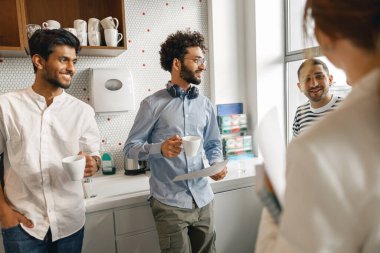 Group of diverse coworkers drink coffee during break and talking about work. Blurred background