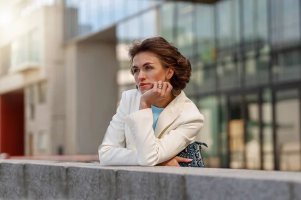 Focused woman in white suit standing near business centre and looking away