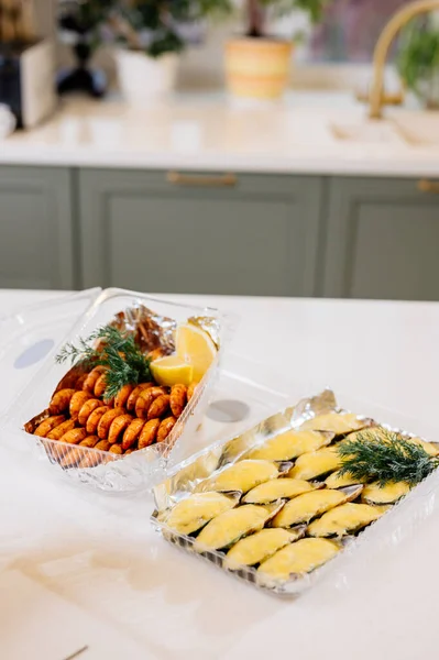 Kabuklu midyeler, plastik bir kutuda peynir ve mutfak masasındaki plastik kutuda kızarmış karidesler.