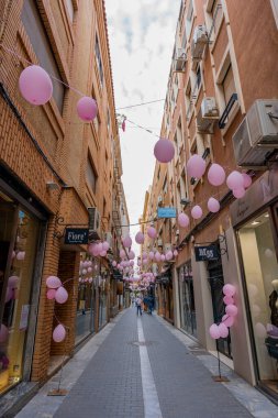 Murcia, İspanya - 16 Ekim 2021: Murcia caddesi kanserle mücadele günü için pembe balonlarla süslenmiş. İnsanlar dükkânın camlarına bakıp yürüyorlar..