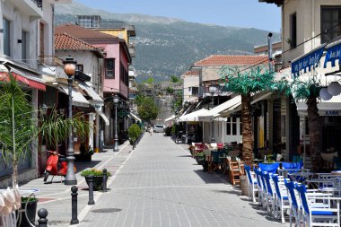 Ioannina, Yunanistan - 01 Temmuz 2021: Yaya bölgesinde çeşitli barlar, dükkanlar ve restoranlar, arka planda eski şehir duvarı bulunan kimliği belirsiz kişiler