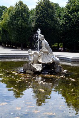 Vienna, Austria - August 01, 2022: Unidentified people rest on bench at western naiad fountain in a rondeau along the tree-lined avenues in the park of former residence of the Habsburg rulers and today a UNESCO World Heritage Site, world-famous touri