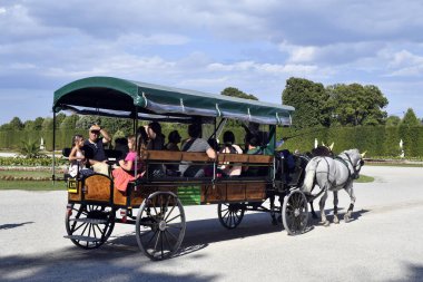 Vienna, Austria - August 01, 2022: Unidentified tourists in a horse-drawn carriage in Schoenbrunn Park- former residence of the Habsburg rulers and today a UNESCO World Heritage Site, world-famous tourist attraction situated in a large park landscape