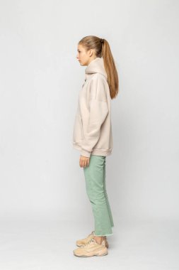 Yeşil kargo pantolonlu ve bej kapüşonlu kız beyaz üzerinde izole edilmiş.