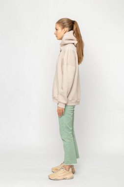 Yeşil kargo pantolonlu ve bej kapüşonlu kız beyaz üzerinde izole edilmiş.
