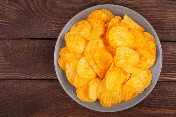 Potato wavy chips in bowl on wooden background, top view.