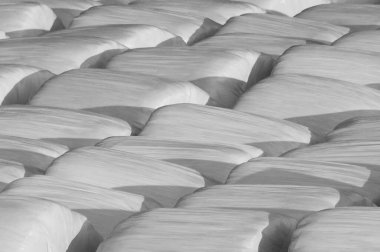 Faded black and white background of plastic wrapped hay bales 