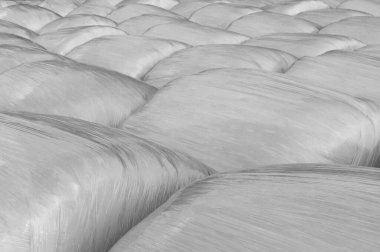 Faded black and white background of plastic wrapped hay bales 