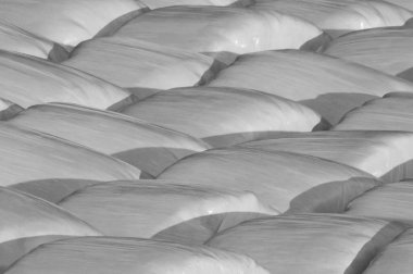Faded black and white background of plastic wrapped hay bales 