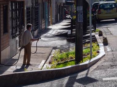 Yaşlı Latin kadın evinin yanındaki küçük yeşil çimenleri suluyor.