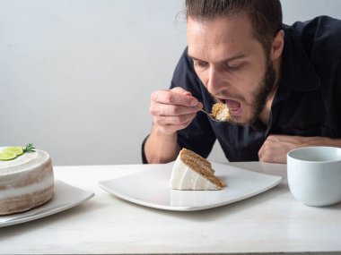 Limonlu, bademli, hindistancevizli, limonlu, tereyağlı, beyaz masadaki kremalı ve beyaz arkaplanlı vejetaryen limonlu kek yiyen bir adam.