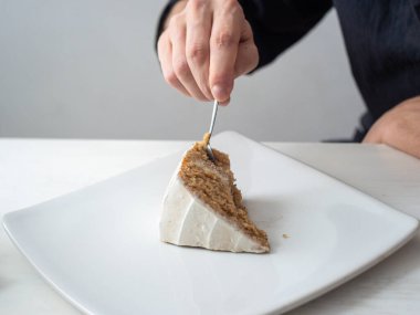 Bir adamın eli bir dilim vejetaryen limonlu keki badem, hindistancevizi ve limonlu krem peynirli tereyağlı beyaz masa ve beyaz arka plan ile keser.