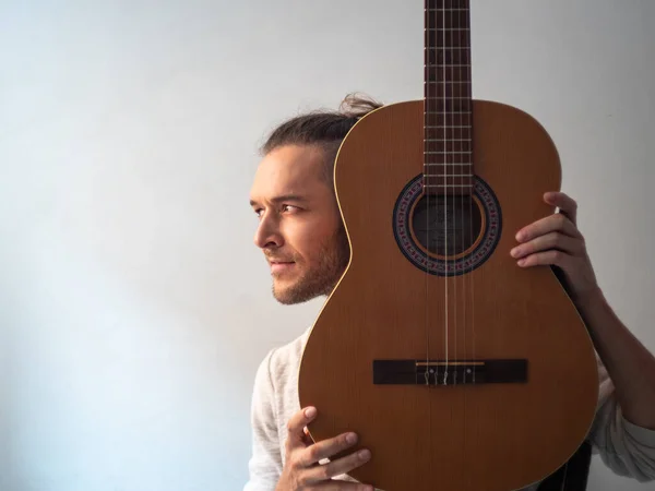 White Man Holds an Acoustic Guitar and Looks at the Camera against a White Background