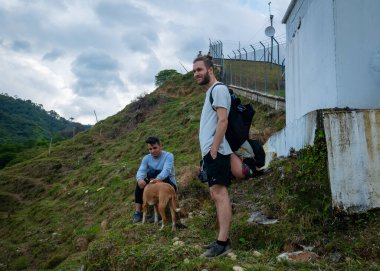 Beyaz adam, Güney Amerikalı bir adamın yanında oturan ve köpeği okşayan manzaranın tadını çıkarıyor.
