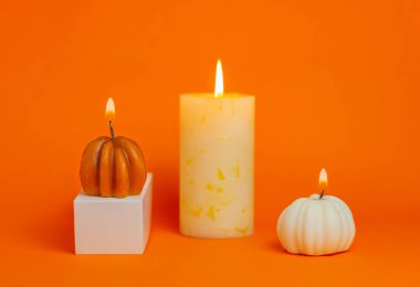 Turuncu arka planda balkabağı şeklinde mum ve mum yakmak. Cadılar Bayramı, Şükran Günü, hasat festivali konsepti