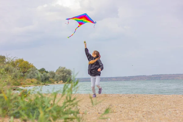 10代の女の子が池の岸に沿って鮮やかなマルチカラーの凧で走ります 屋外活動と健康的なライフスタイルの概念は — ストック写真