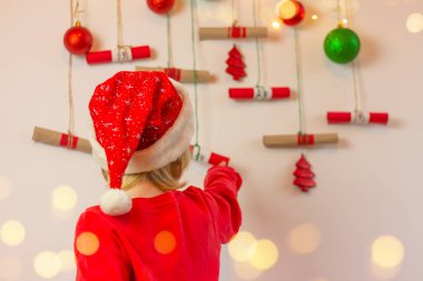 Noel Baba şapkalı çocuk duvarda asılı duran yeni yıl takvimine yakın bir yerde. Noel hazırlama konsepti