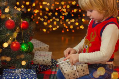 Çocuk Noel ağacının yanında bir hediye paketini açıyor. Noel ve yeni yıl, çocukluk, tatil konsepti