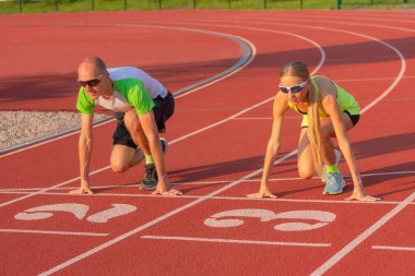 Stadyumdaki atletik kadın ve erkek koşuya hazırlanıyor. Spor, eğitim ve sağlıklı yaşam tarzı, cinsiyetler arasındaki rekabet ve eşitlik kavramı.