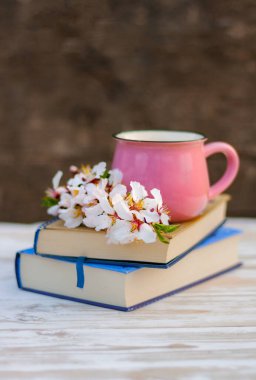 Badem ağacının çiçek açan bahar dalı ve masanın üzerindeki kitap yığınının üzerindeki pembe bardak.