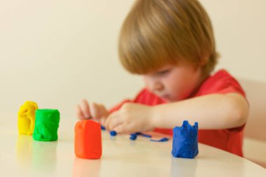 Çocuk çocuk masada oturuyor ve çocuk sınıflarında çok renkli plastiklerin heykellerini yapıyor.