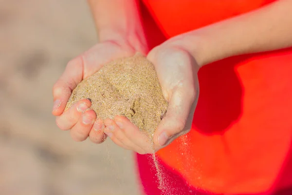 close-up of a handful of sand in the hands of a young woman on the background of the sea beach.