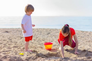 Erkek ve kız deniz kenarında oyuncaklarla oynarken eğleniyorlar. Kardeş kavramı, çocukluk, yaz tatili ve aktiviteler