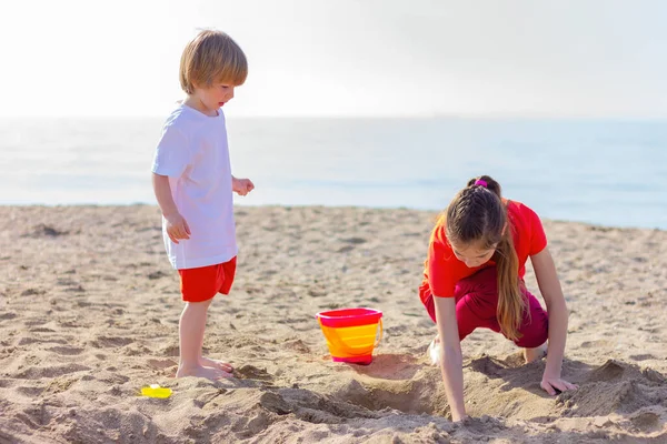 Erkek ve kız deniz kenarında oyuncaklarla oynarken eğleniyorlar. Kardeş kavramı, çocukluk, yaz tatili ve aktiviteler